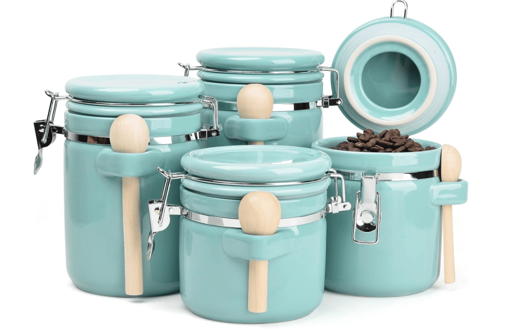 A set of four turquoise ceramic storage jars with wooden scoops, featuring metal clamps and one jar with coffee beans inside.
